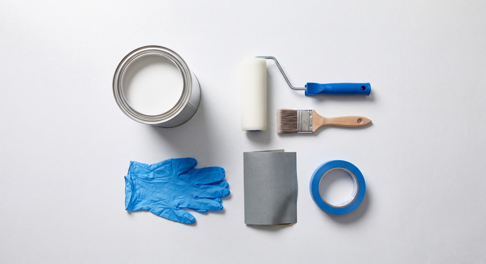 Flat lay of cold room panel painting supplies — epoxy paint, foam roller, brush, gloves, sandpaper and masking tape